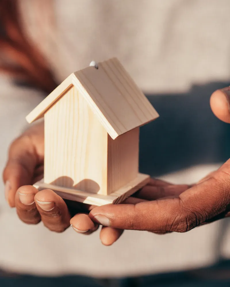 Mani che proteggono un modellino di casa in legno - ristrutturazione del debito per salvare la casa
